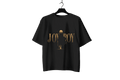 A black short-sleeve t-shirt hanging on a black hanger against a dark background, featuring a gold graphic print on the front with the text 'JOY BOY' and a stylized figure.