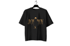 A black short-sleeve t-shirt hanging on a black hanger against a dark background, featuring a gold graphic print on the front with the text 'JOY BOY' and a stylized figure.